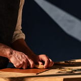 Hands burnishing the edges of a leather folio at a workbench