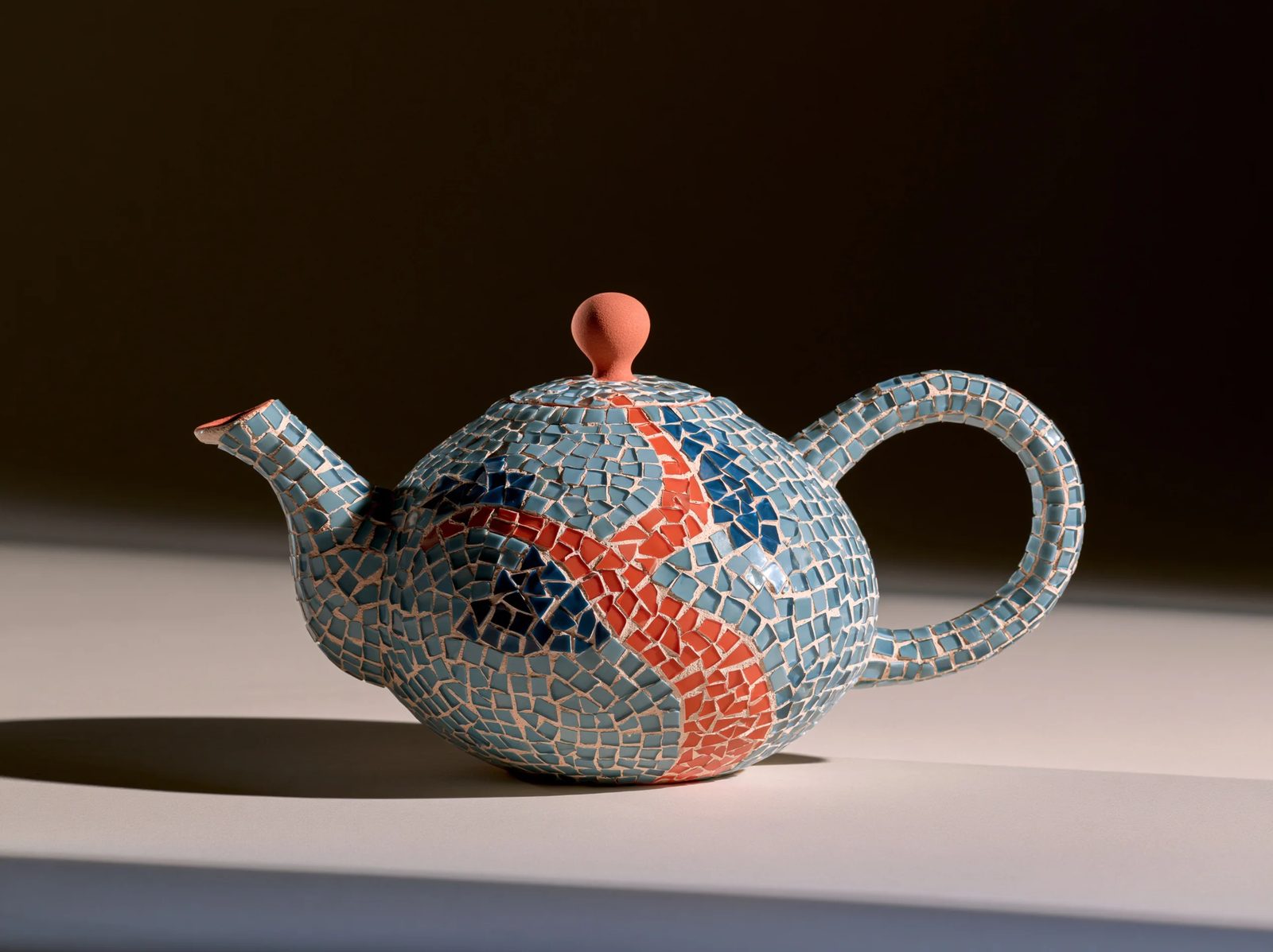 a ceramic teapot covered in mosaic, small glass tesserae arranged in a pattern, visible grout lines, muted blue and terracotta tones, soft studio light on a plain background --ar 1:1 --style raw --s 50