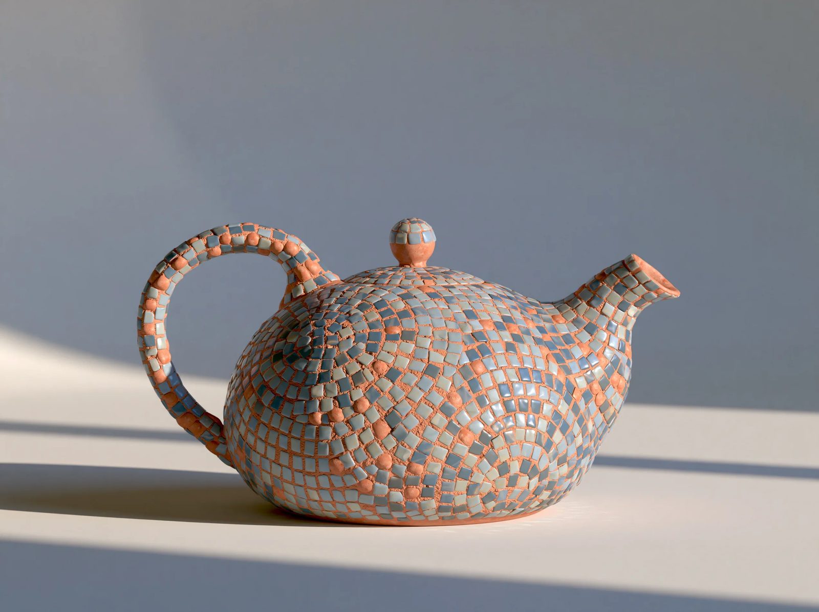 a ceramic teapot covered in mosaic, small glass tesserae arranged in a pattern, visible grout lines, muted blue and terracotta tones, soft studio light on a plain background --ar 1:1 --style raw --s 50