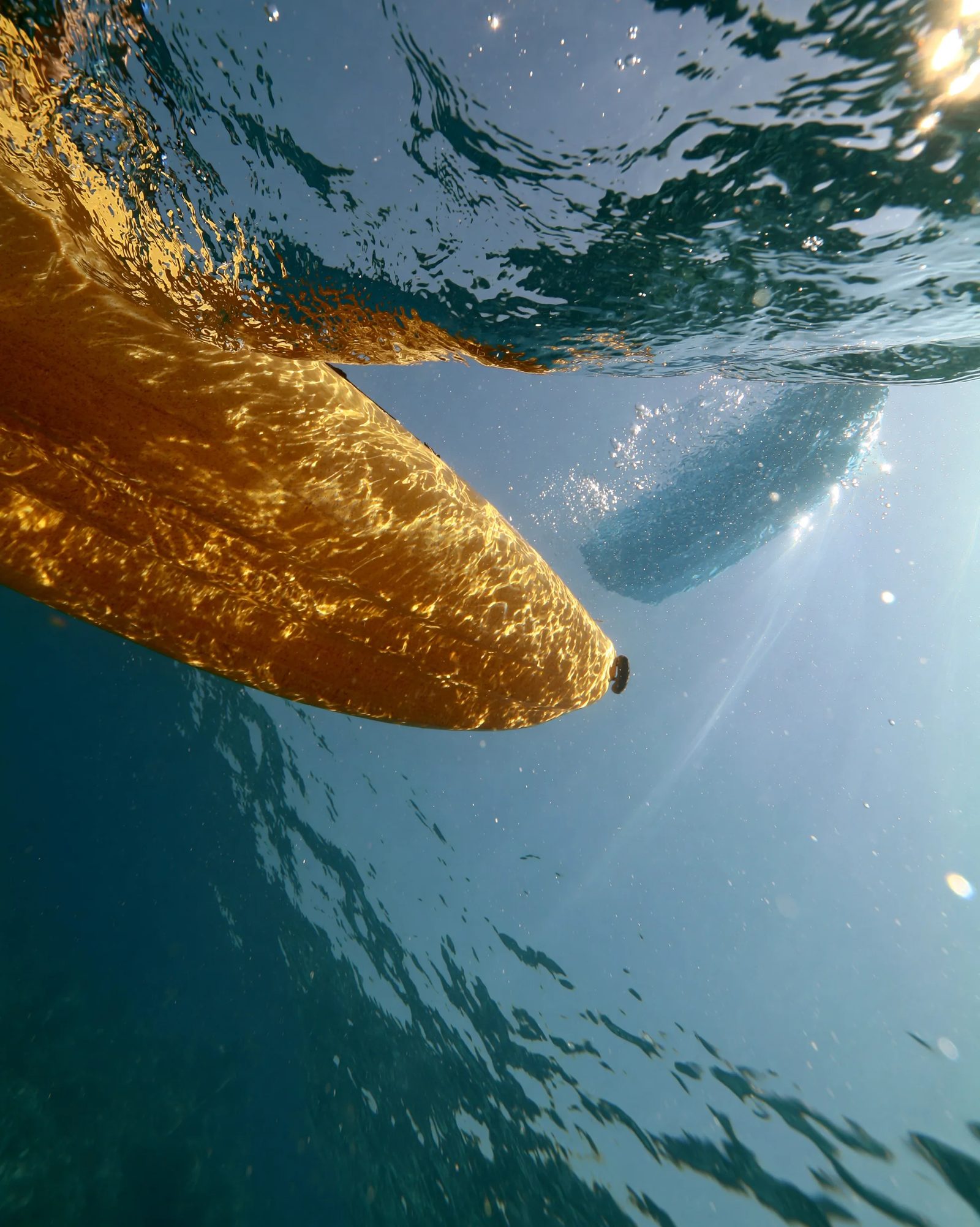 Underwater top-view, looking up from beneath the surface at a pear yellow kayak floating above, water surface distorted with ripples, sunlight streaming down creating caustic patterns on the hull, clear blue water --ar 4:5 --style raw --s 50 --preview