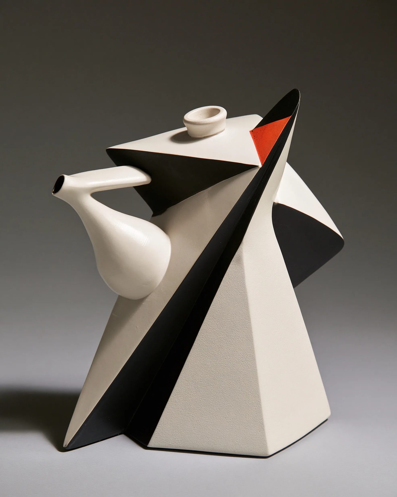 a white ceramic teapot in vorticism, hard diagonal facets slicing the ceramic body, converging sharp planes, stark black and white with rust accent, machine-age geometric abstraction, graphic flat light --ar 4:5 --style raw --s 50 --preview
