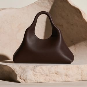 A sculptural leather handbag sits elegantly against a soft, matte alabaster backdrop in a minimalist studio setup.