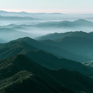 A wide panoramic view of rolling mountain ridges receding into the horizon, demonstrating atmospheric perspective as each successive layer becomes lighter and bluer.