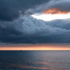 A seascape with bisected composition, the horizon line splitting the frame evenly between stormy sky and choppy water, with a small solitary boat on the dividing line.