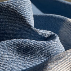 Macro close-up of a denim swatch, showing the diagonal twill weave, indigo dye with white weft specks, and subtle fading at the edges.