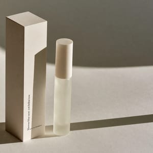 A set of minimalist cosmetic embalagens featuring a matte-cream paper box and a frosted-glass bottle with elegant black typography.