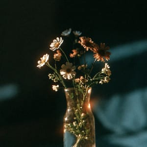 A glass vase holding wildflowers, lit softly, displaying the faded, warm color shifts and heavy grain characteristic of expired film.