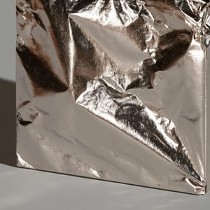 A minimalist packaging box wrapped in crinkled silver foil, showing sharp reflections under studio lighting.