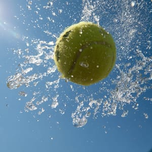 A wet yellow tennis ball spinning in mid-air, shot with a freeze-motion shutter at 1/8000s, water droplets radiating off its surface suspended in mid-flight with zero motion blur and razor-sharp detail, bright direct sunlight --ar 4:3 --raw --profile 9qzq3j7 --stylize 50 --preview