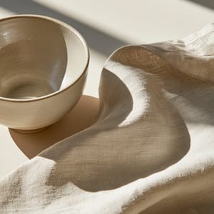 A minimalist ceramic vessel on a wooden surface rendered in a soft greige palette of muted taupe and grey.