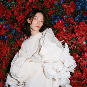 A woman in neutral beige standing in front of a hyper-saturated floral backdrop in a brightly lit photography studio.
