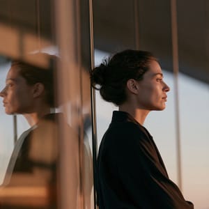 A soft profile of a woman seen through multiple window panes, creating a complex layered glass reflection in muted dusk light.