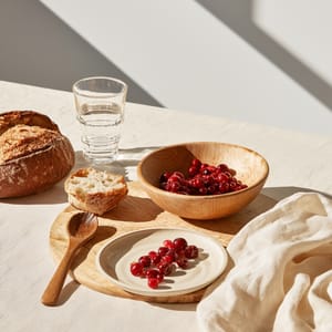 A minimalist room setup showcasing a lingonberry red palette on a ceramic cup resting atop a pale wooden stool.