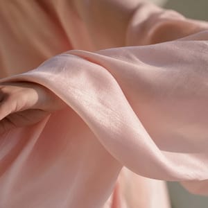 A classical silk hanfu robe in delicate lotus pink draped elegantly against a minimalist, soft white background.