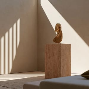 A luxury boutique interior featuring minimal plaster walls, a single travertine display plinth, and warm ambient light.