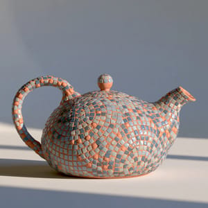 a ceramic teapot covered in mosaic, small glass tesserae arranged in a pattern, visible grout lines, muted blue and terracotta tones, soft studio light on a plain background --ar 1:1 --style raw --s 50