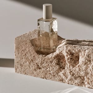 A minimalist glass skincare bottle nestled inside a textured packaging block made of cream-colored mycelium foam.