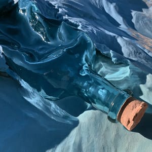 A glass bottle half-buried in sand, its surface reflecting an Oceanic palette of deep teal and aquamarine against cool blue-gray grains.