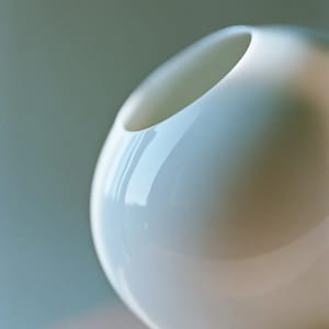 A smooth white porcelain vase with a delicate translucency, lit by soft diffused light against a pale background.