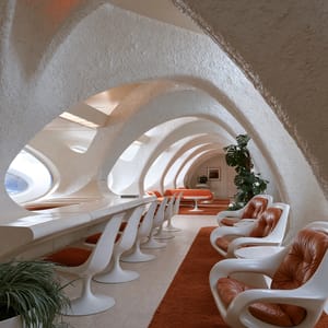 An organic retro-futuristic lounge showcases classic Space Age design with white curved arches, pedestal armchairs, orange cushions, and circular windows.
