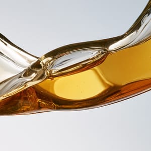 A close-up macro shot of a thick golden serum drop displaying viscous shear as it stretches smoothly across a glass plate.
