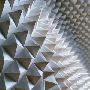 An abstract design featuring the visual repetition of delicate, folded white paper pyramids creating a wave-like pattern.