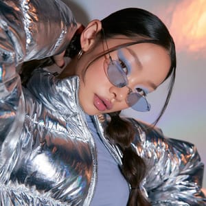 A young Korean woman posing in a shiny silver jacket and tinted sunglasses captures the vibrant Y2K aesthetic.