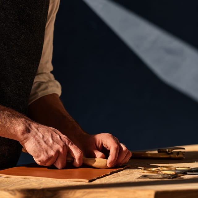 Hands burnishing the edges of a leather folio at a workbench