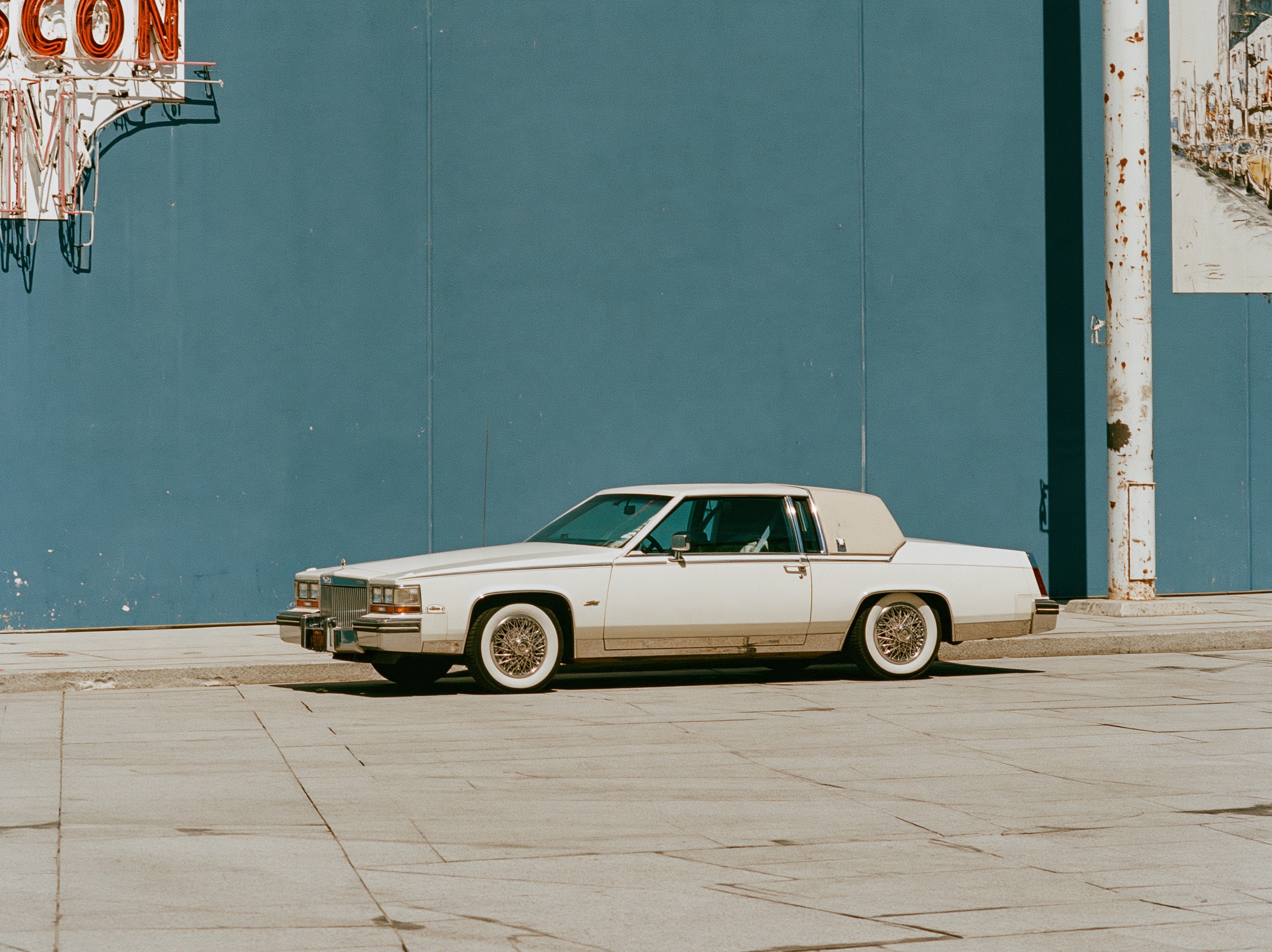 A 1980s sedan illuminated by bold neon lighting at dusk.