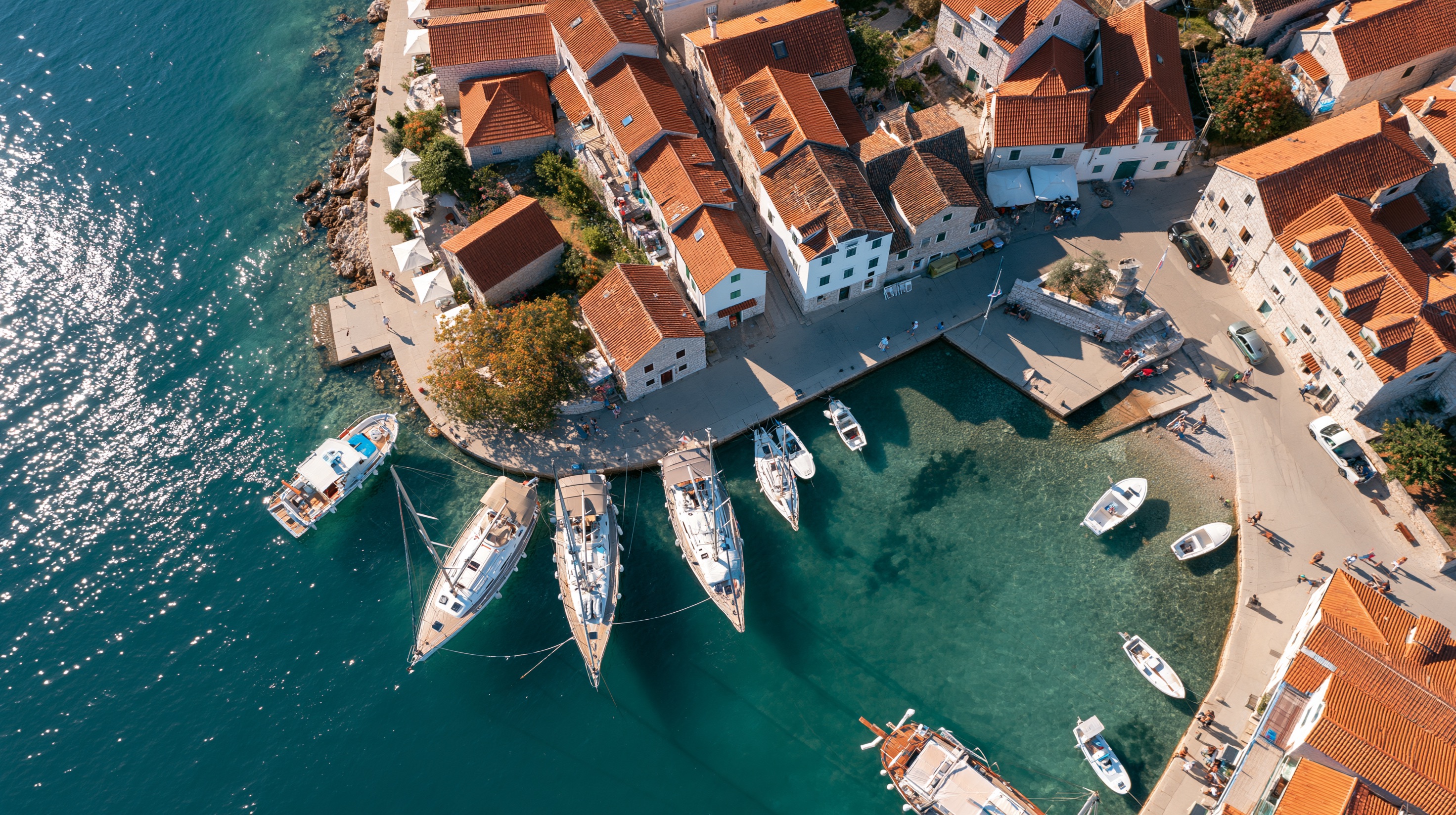 An aerial view looks straight down on a small harbour town, its quays and rooftops packed between water and shore.