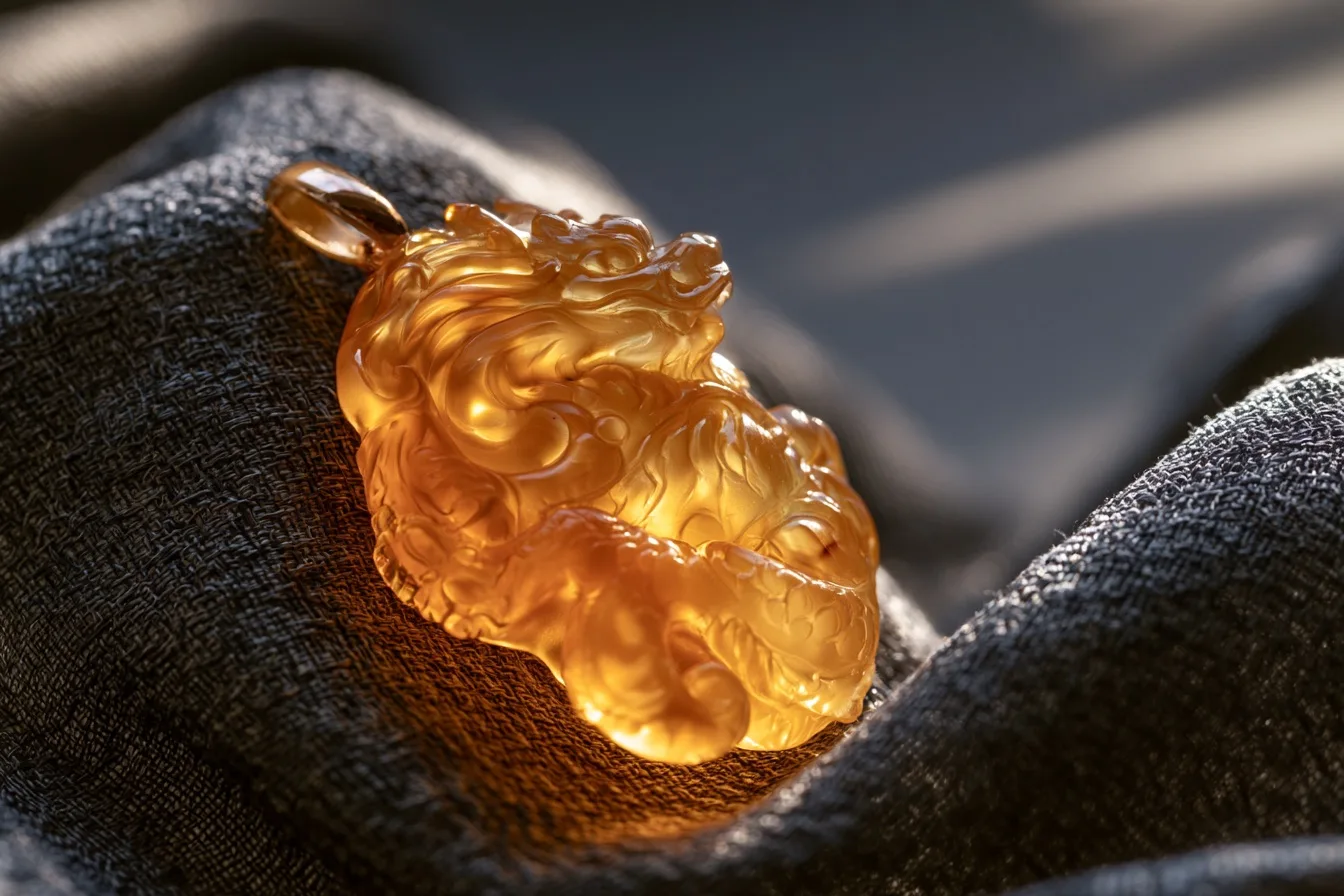 A detailed close-up of a carved dragon pendant glowing with a rich, translucent amber yellow color against a dark backdrop.