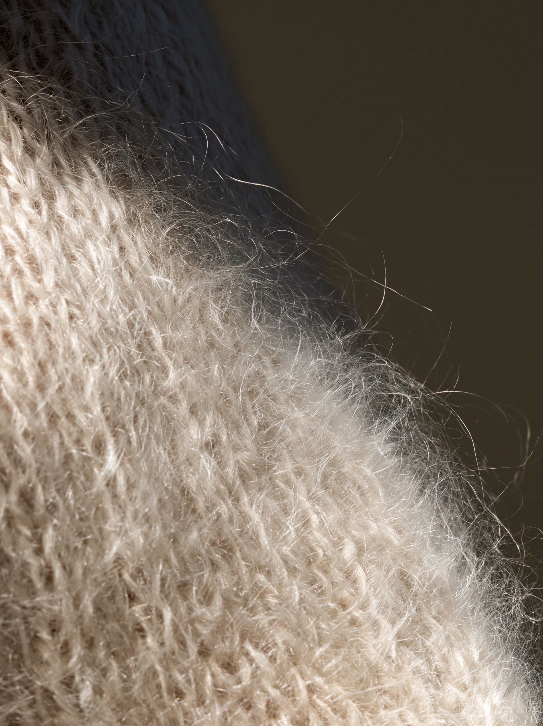 A close-up of an oversized sweater knitted from brushed mohair, showing fine fuzzy fibers glowing in warm side light.