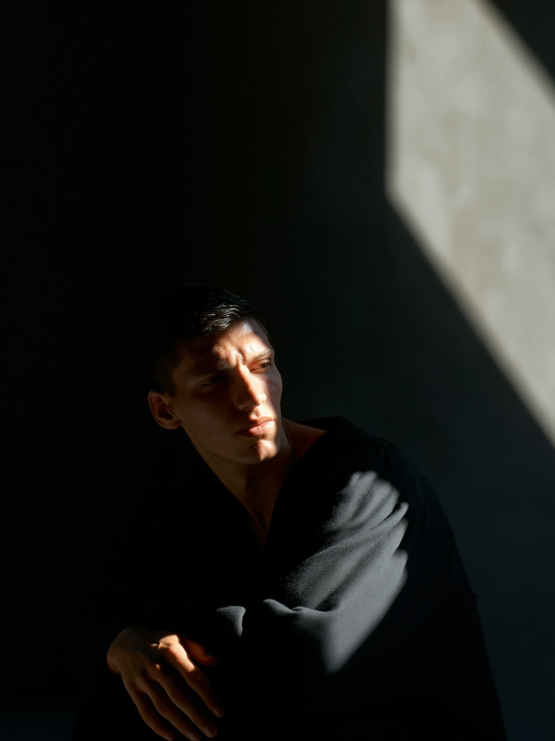 A solitary figure in a dim room, their face half-lit by a single shaft of window light, a stark demonstration of chioroscuro.