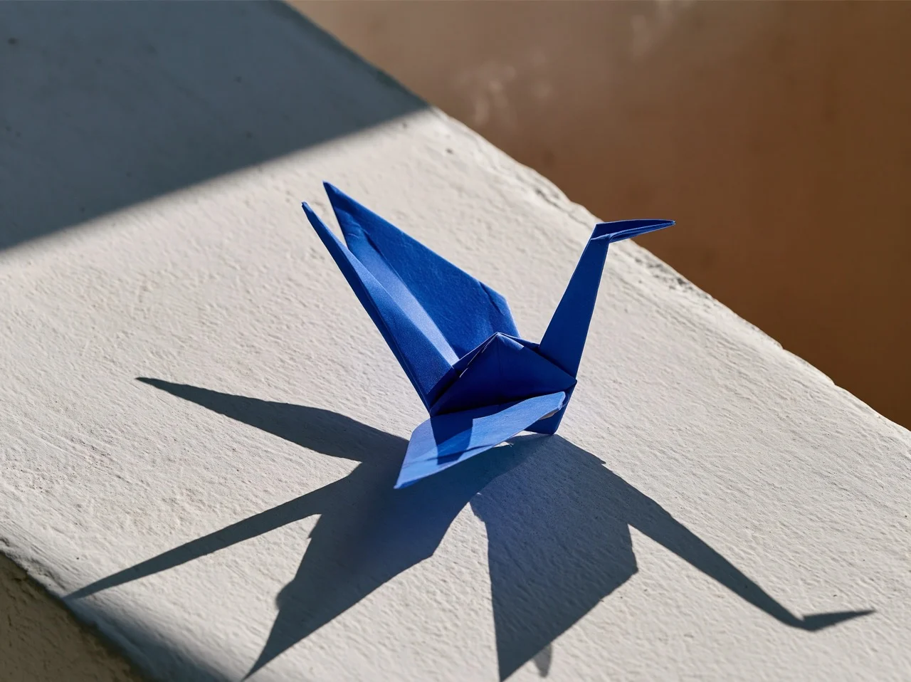 A sharp origami paper bird folded in striking cobalt blue, resting on a smooth pale gray concrete surface.