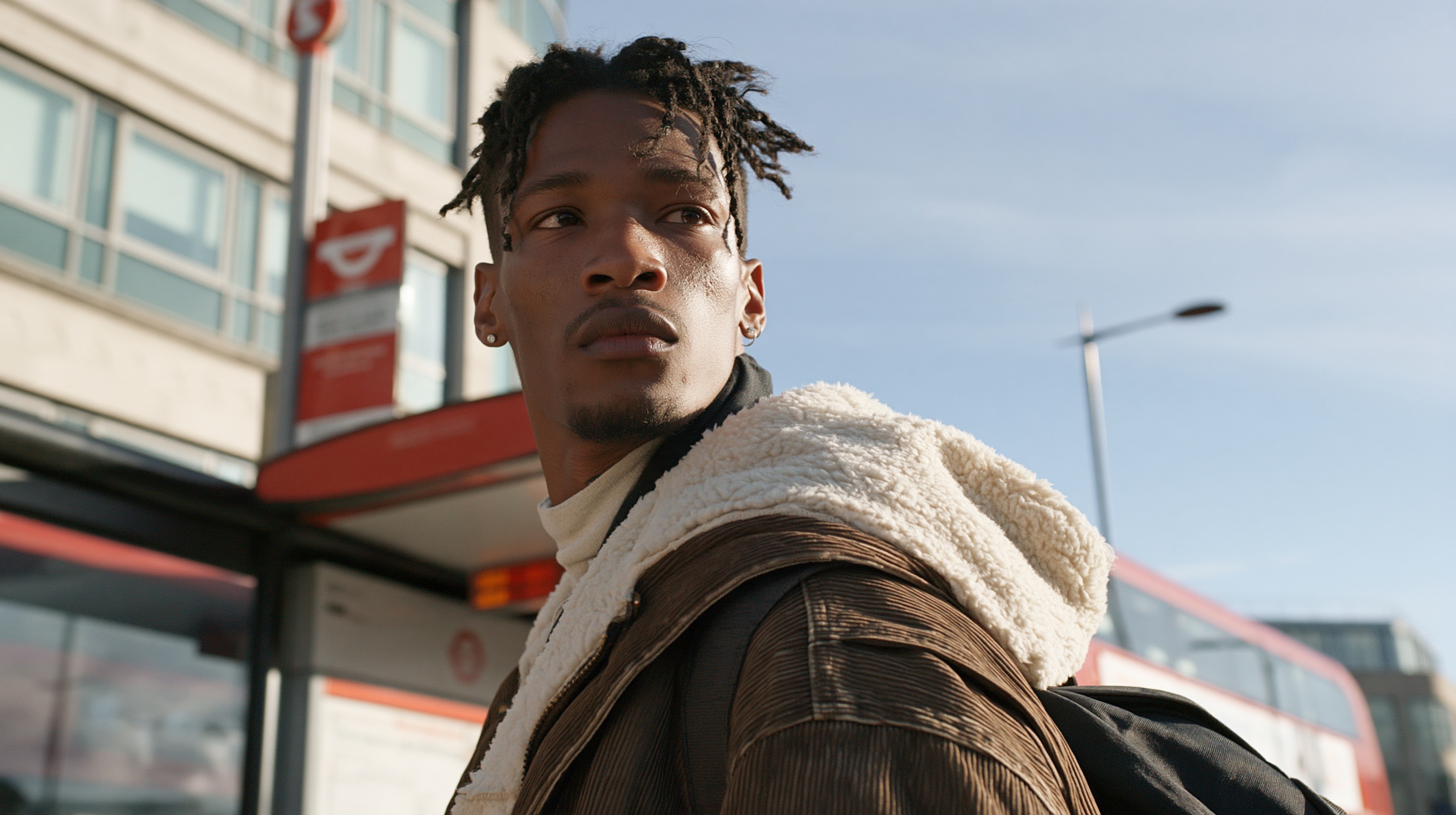 A film still shows a man standing at a bus stop, looking down the empty street.