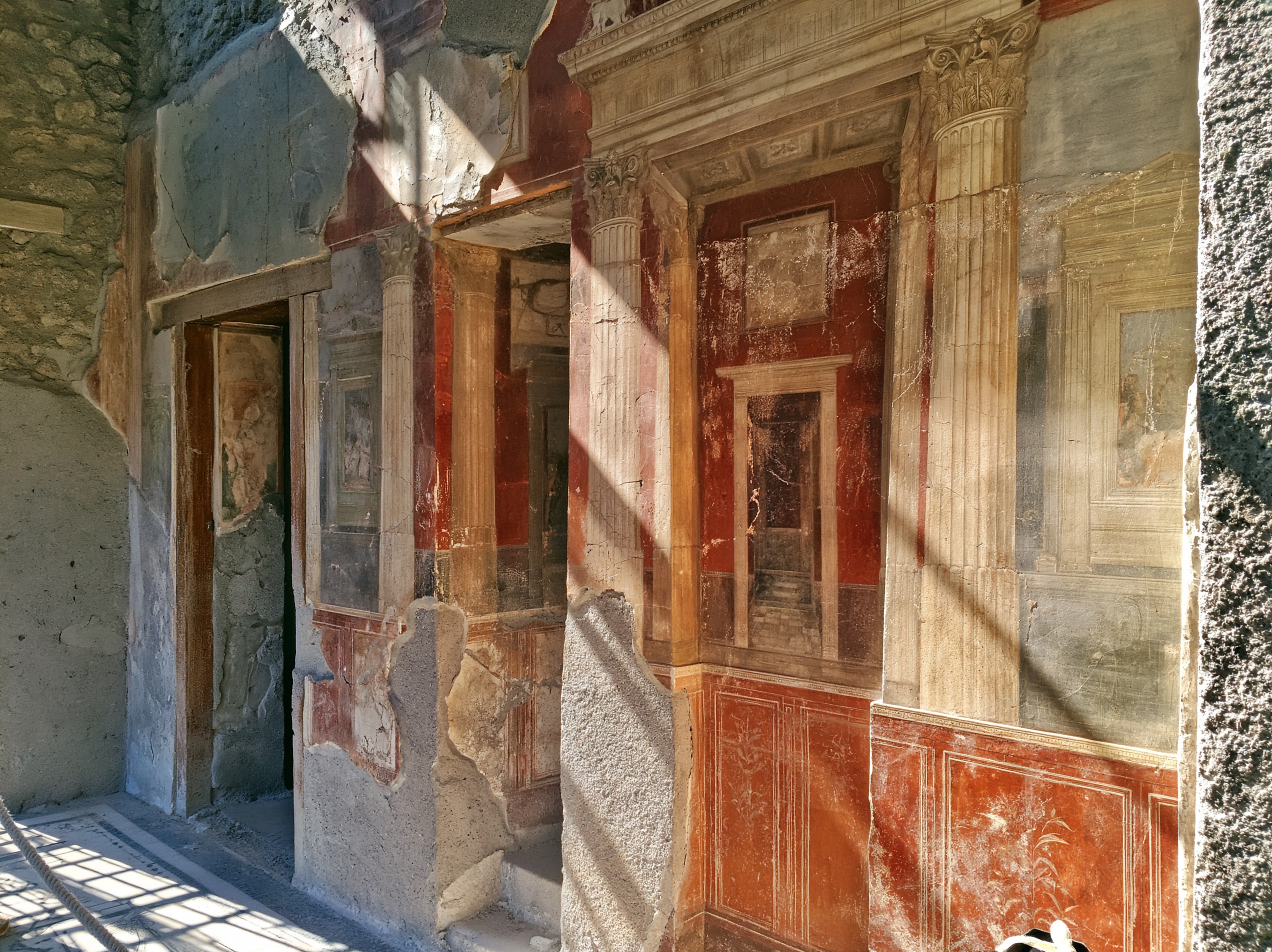 A wall shows fourth style art with painted columns opening onto shallow rooms.