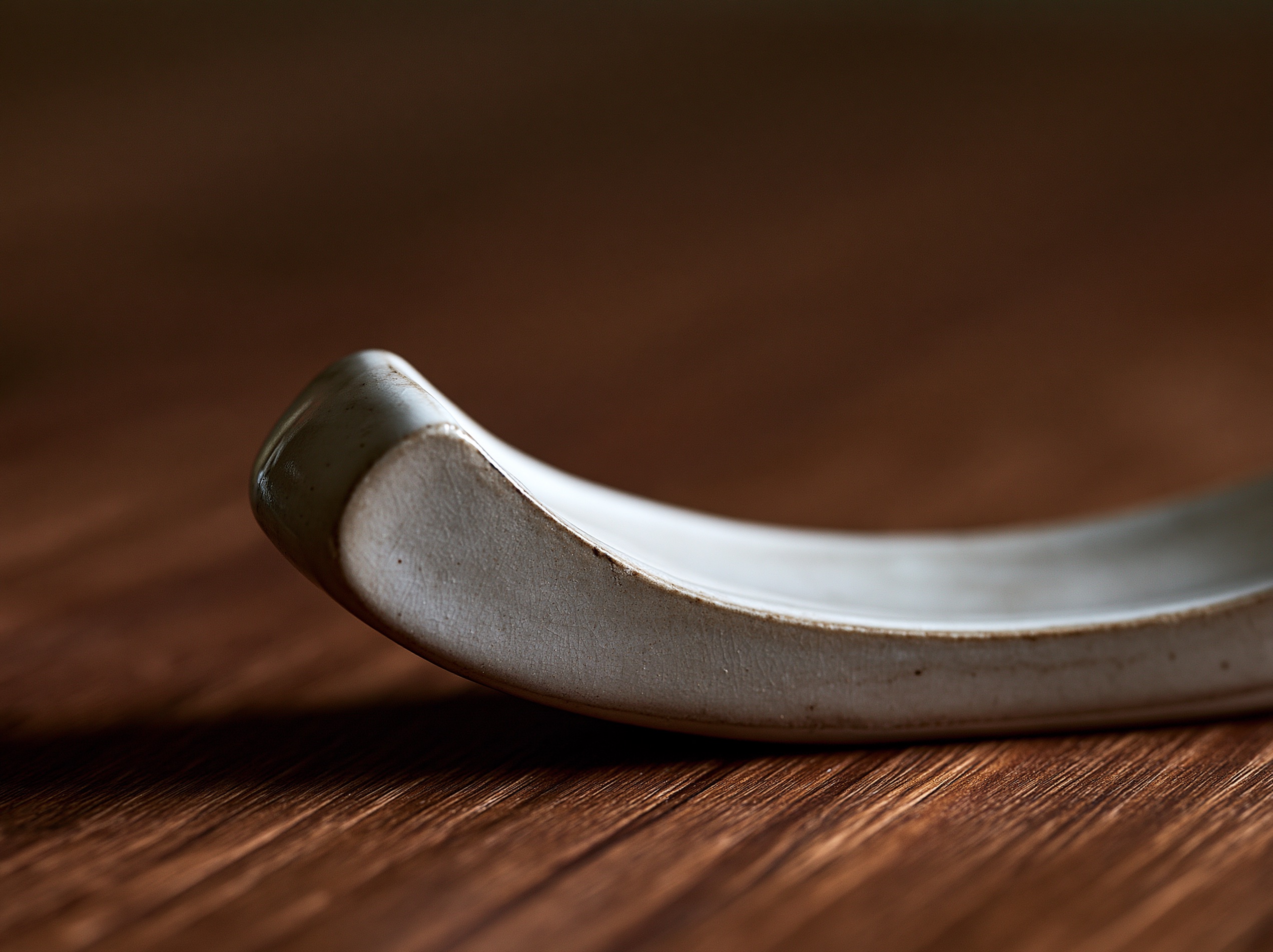 A close-up of a glazed ceramic hashioki resting beside a dark linen napkin on a natural wooden dining table.