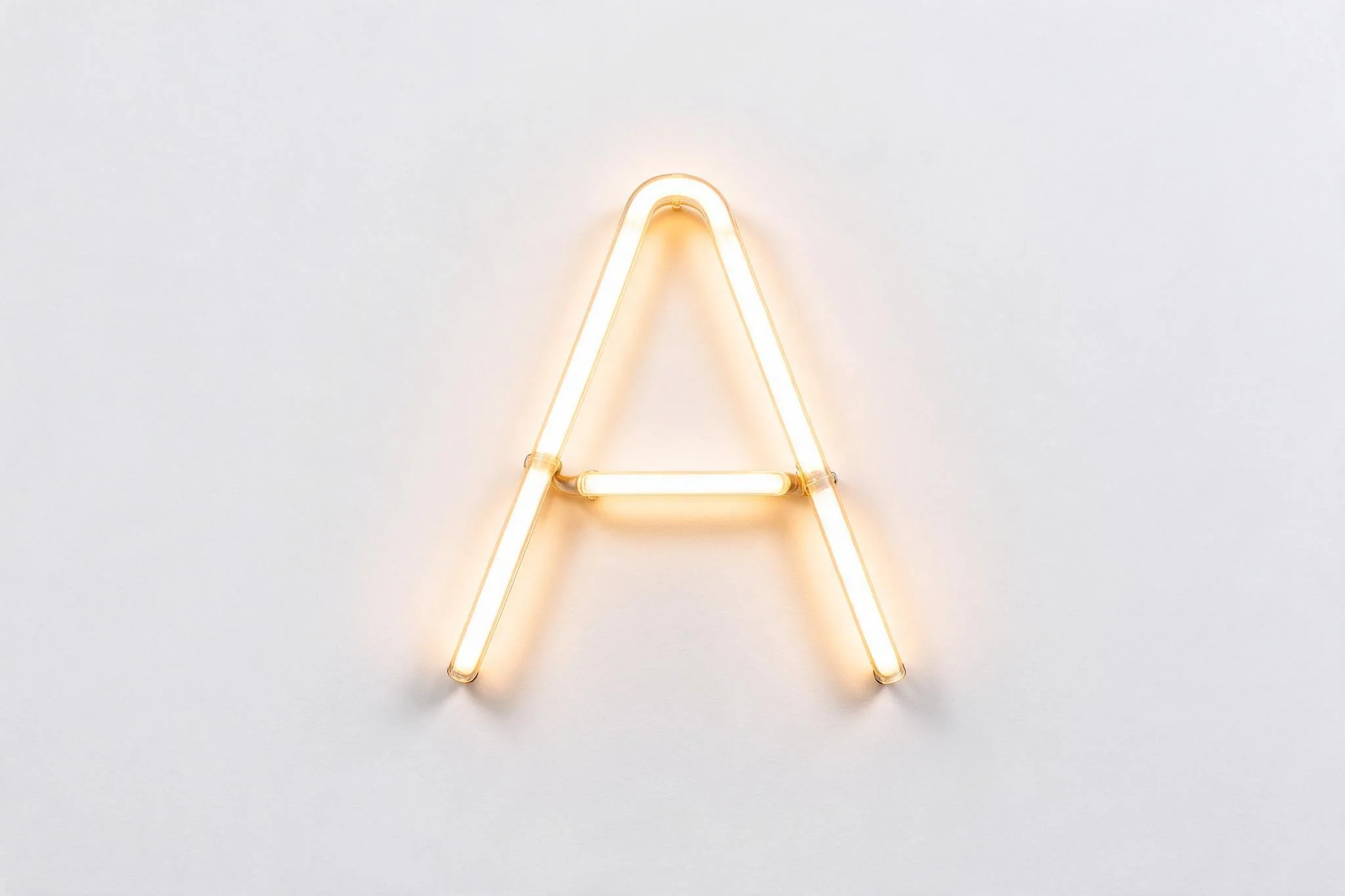 The letter A formed from a bent neon tube in warm white light on a pure white background