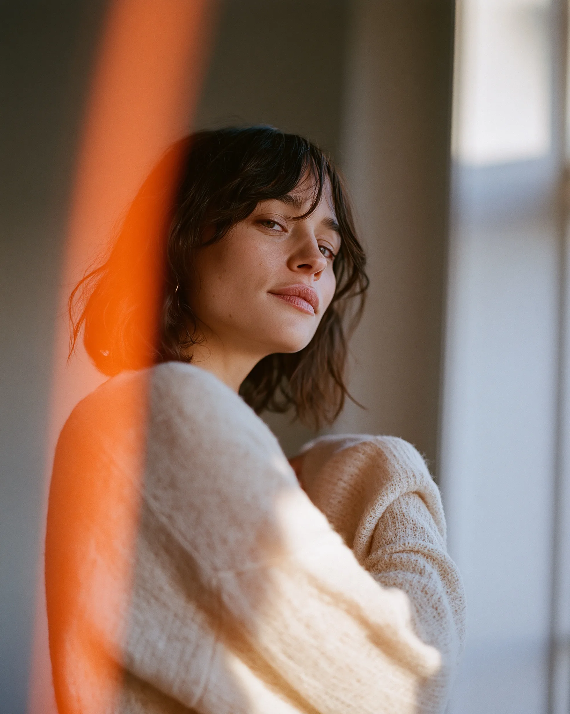 A warm, orange light leak washes across a quiet portrait of a woman looking out a window, creating a nostalgic haze.