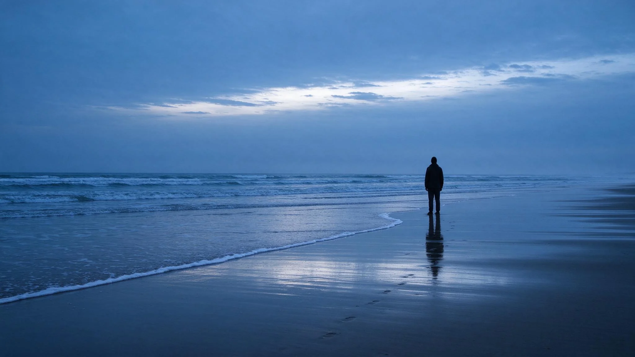 A long shot shows a lone figure standing on a beach, tiny against the sand and the sea.