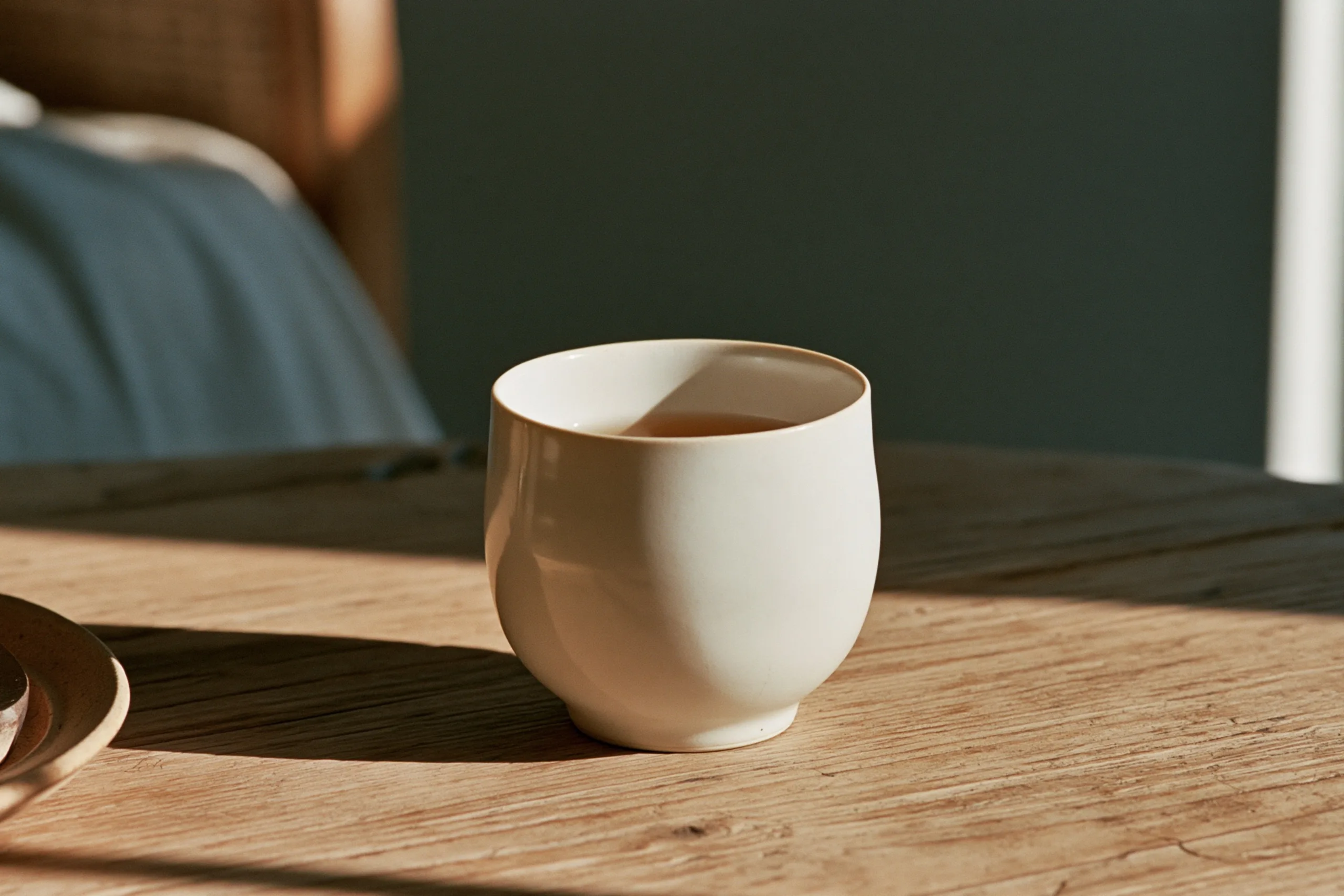 Soft daylight catches a white ceramic cup of tea, casting gentle milky highlights across its glazed surface.