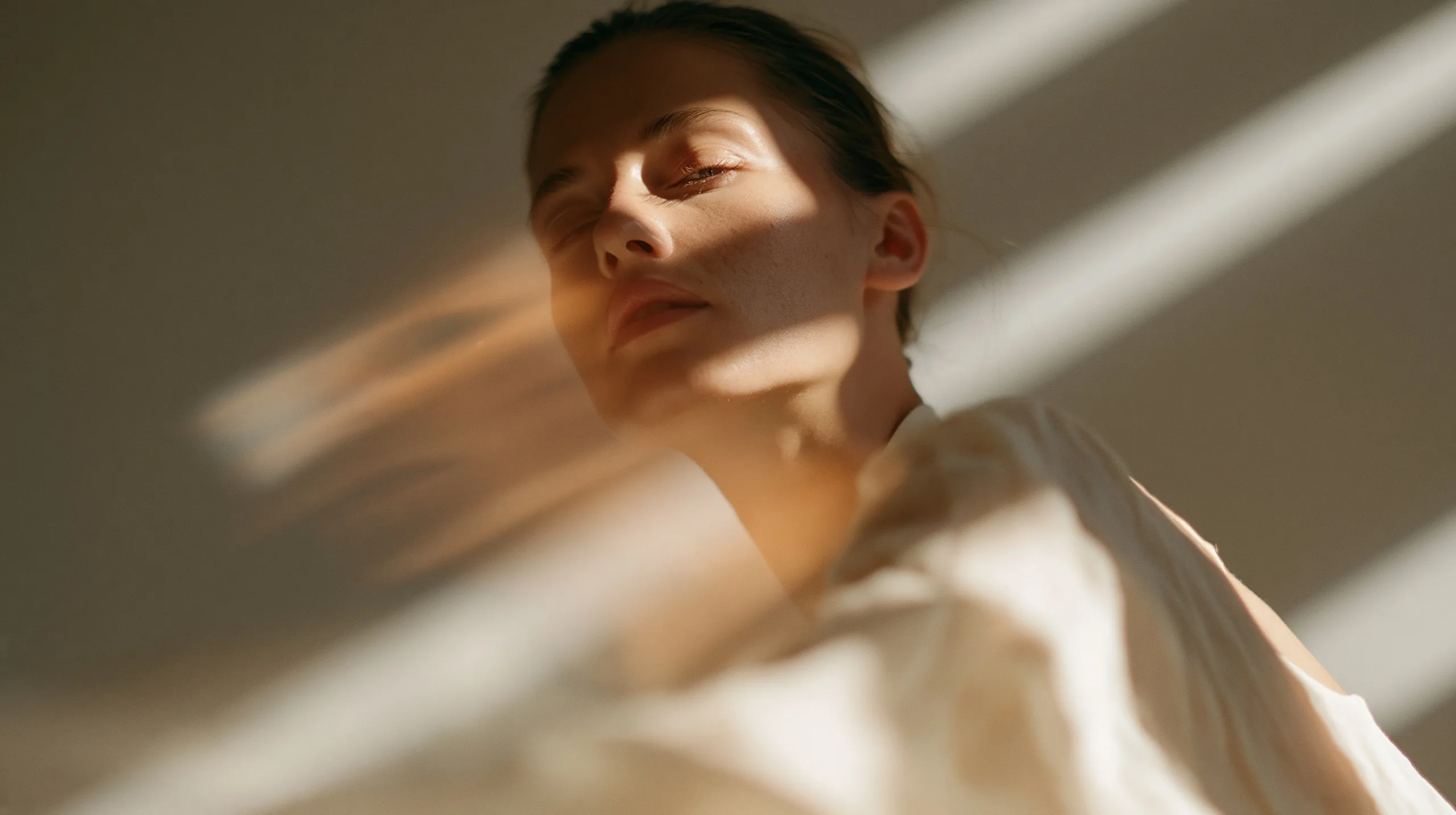 A quiet portrait of a woman rendered as a nebulous holographic projection floating in a dimly lit, minimalist room with warm, dusty particles.
