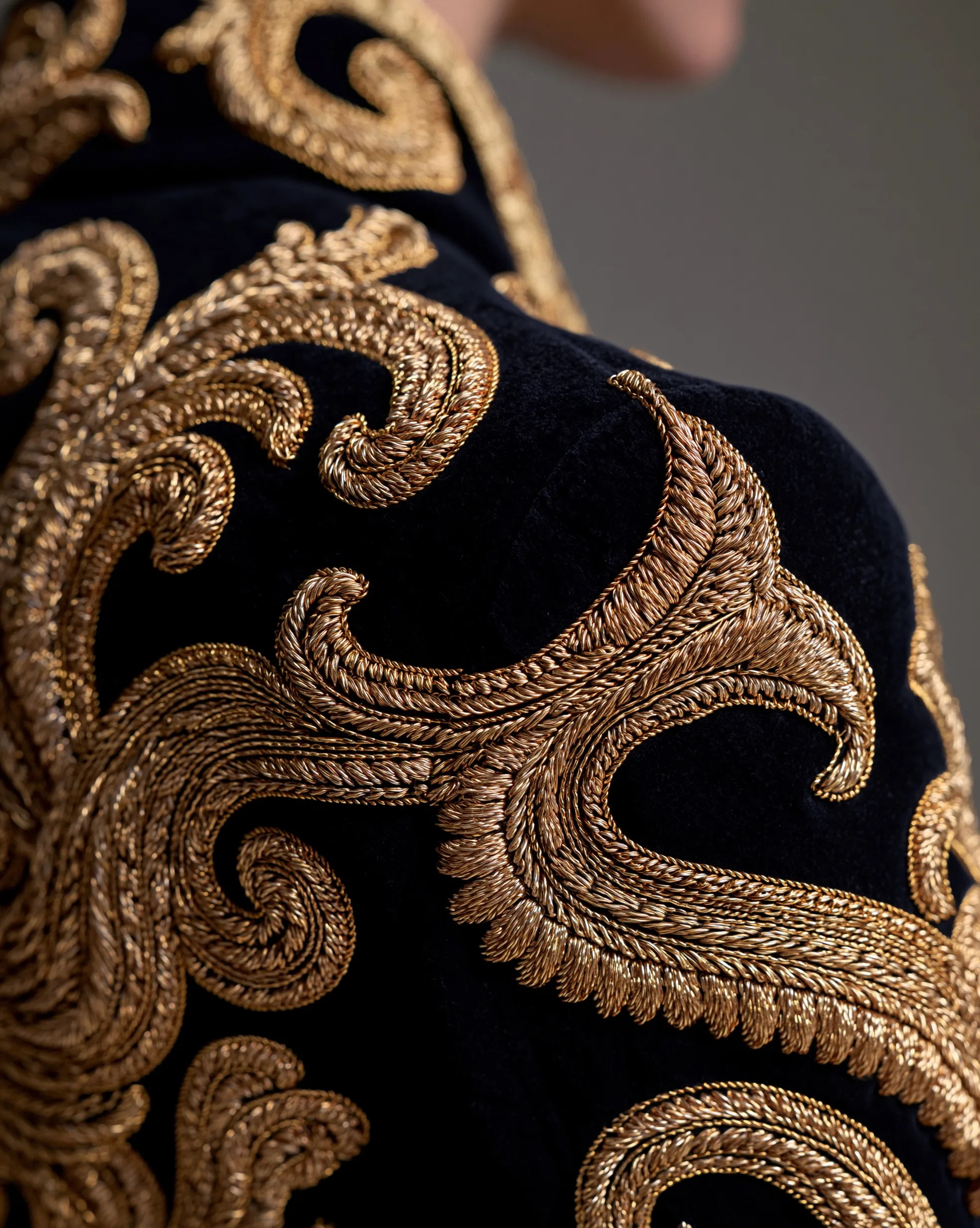 Close-up of a black velvet haute couture jacket adorned with ornate gold embroidery reflecting soft studio light.