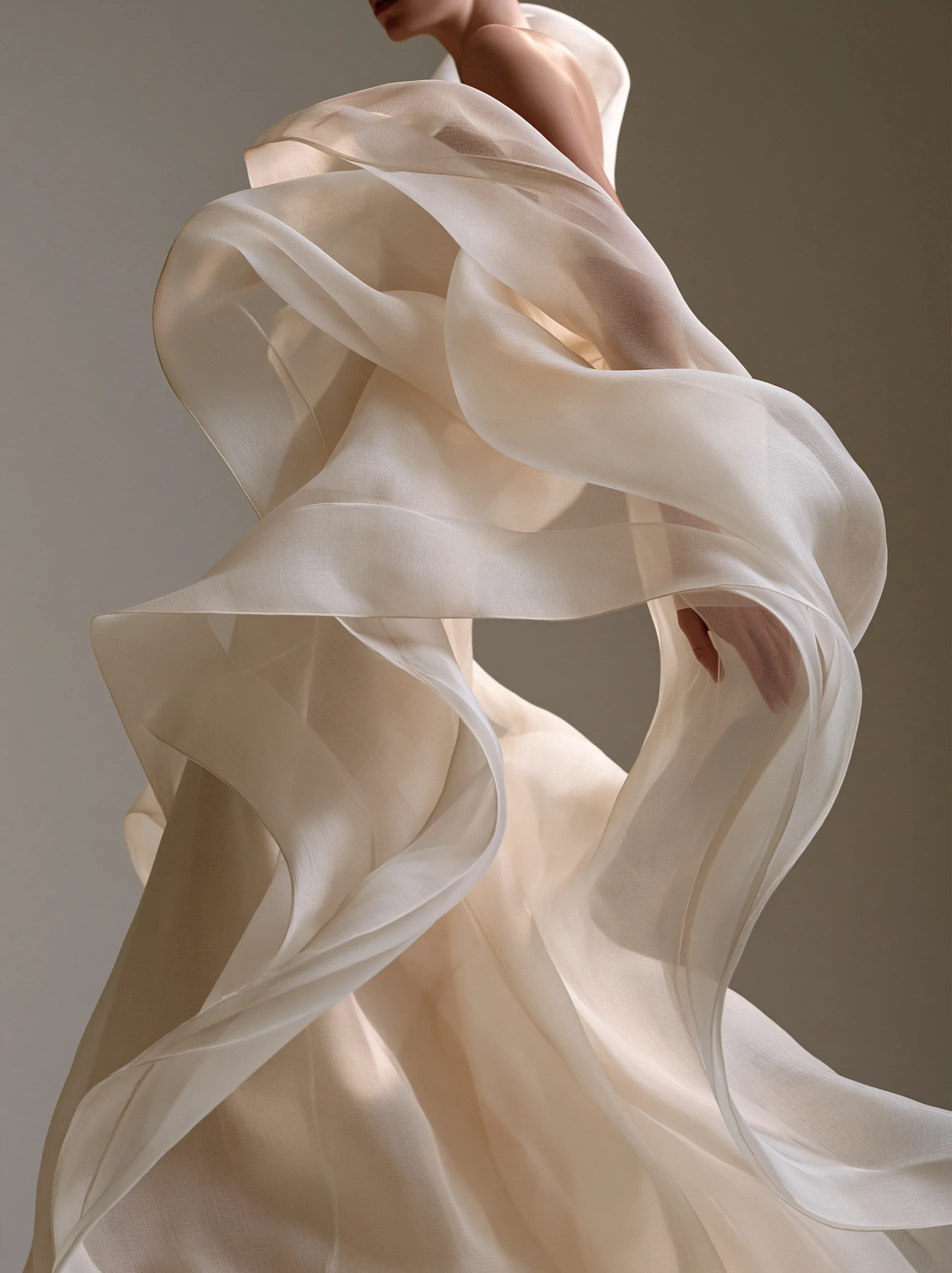 A draped minimalist haute couture gown made of pale beige sheer organza, catching soft, diffused studio light.