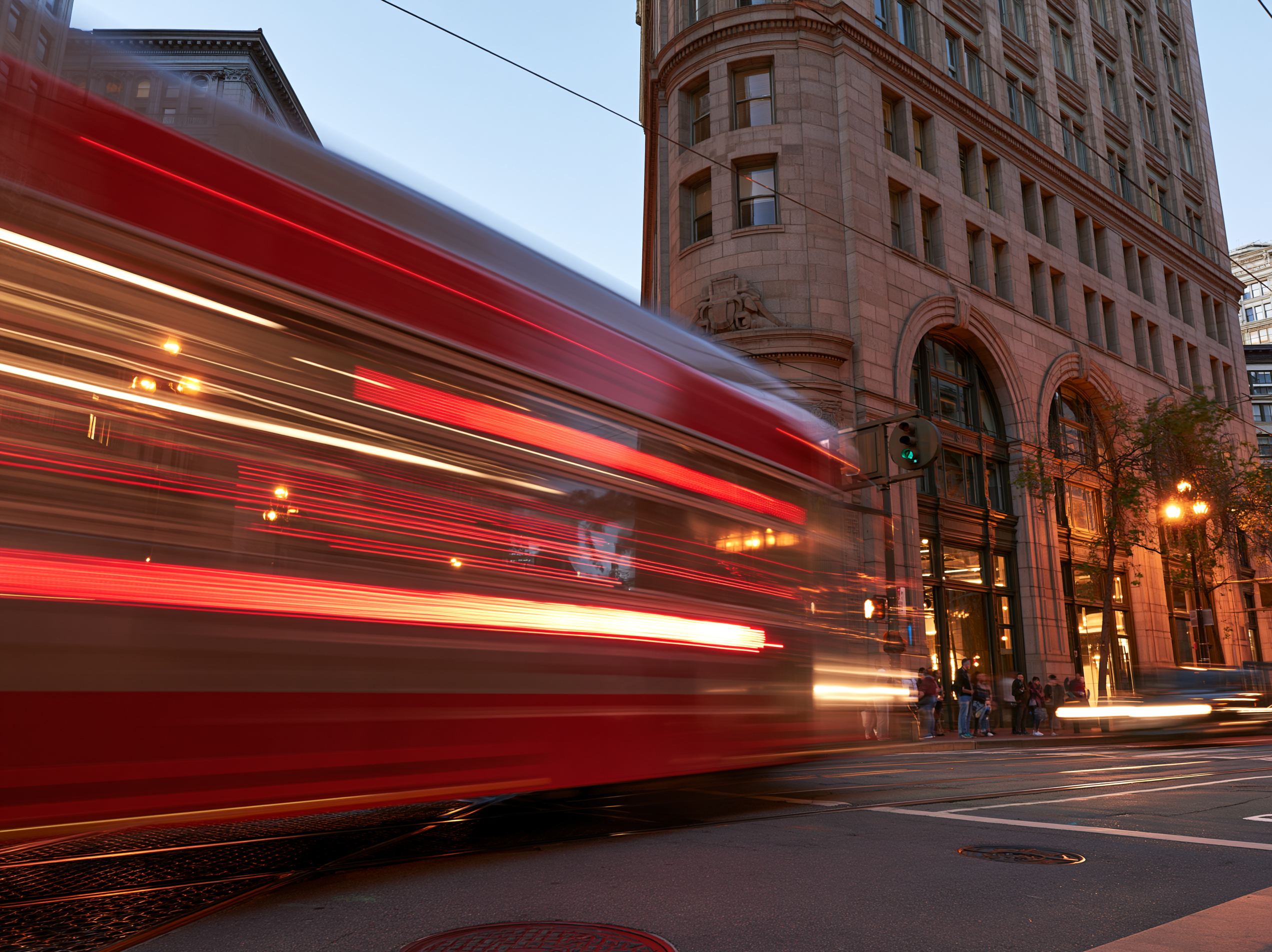 A red city bus smears into light trails around a sharp stone corner, captured with shutter drag at dusk.