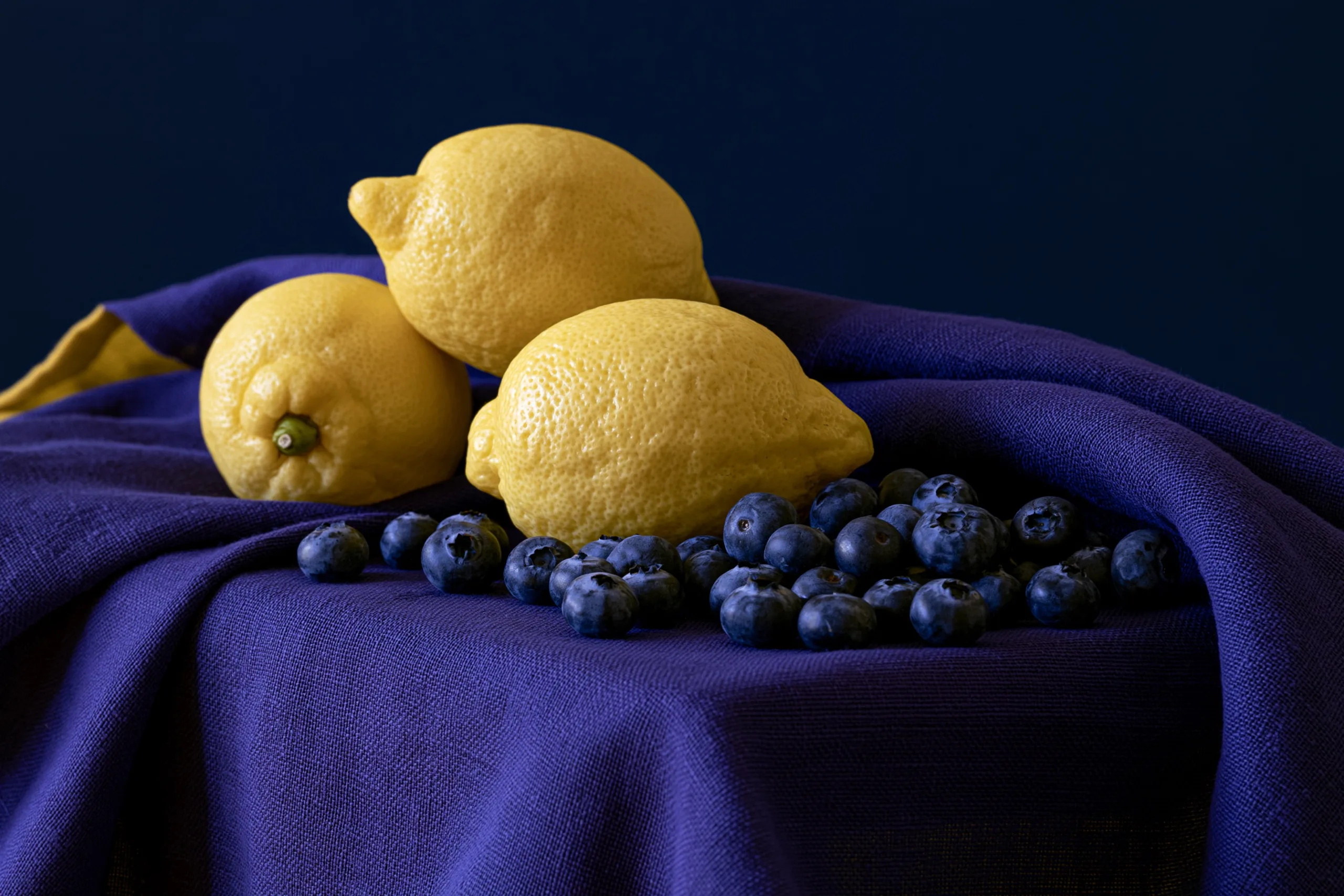 A still life of lemons and blueberries on a violet cloth, demonstrating split-complementary color with yellow set against blue-violet and red-violet accents.