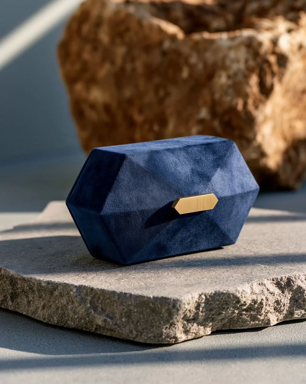 A geometric midnight blue clutch purse featuring a velvety matte finish that absorbs light, creating soft shadow gradients without hard highlights, accented by a brushed gold clasp.