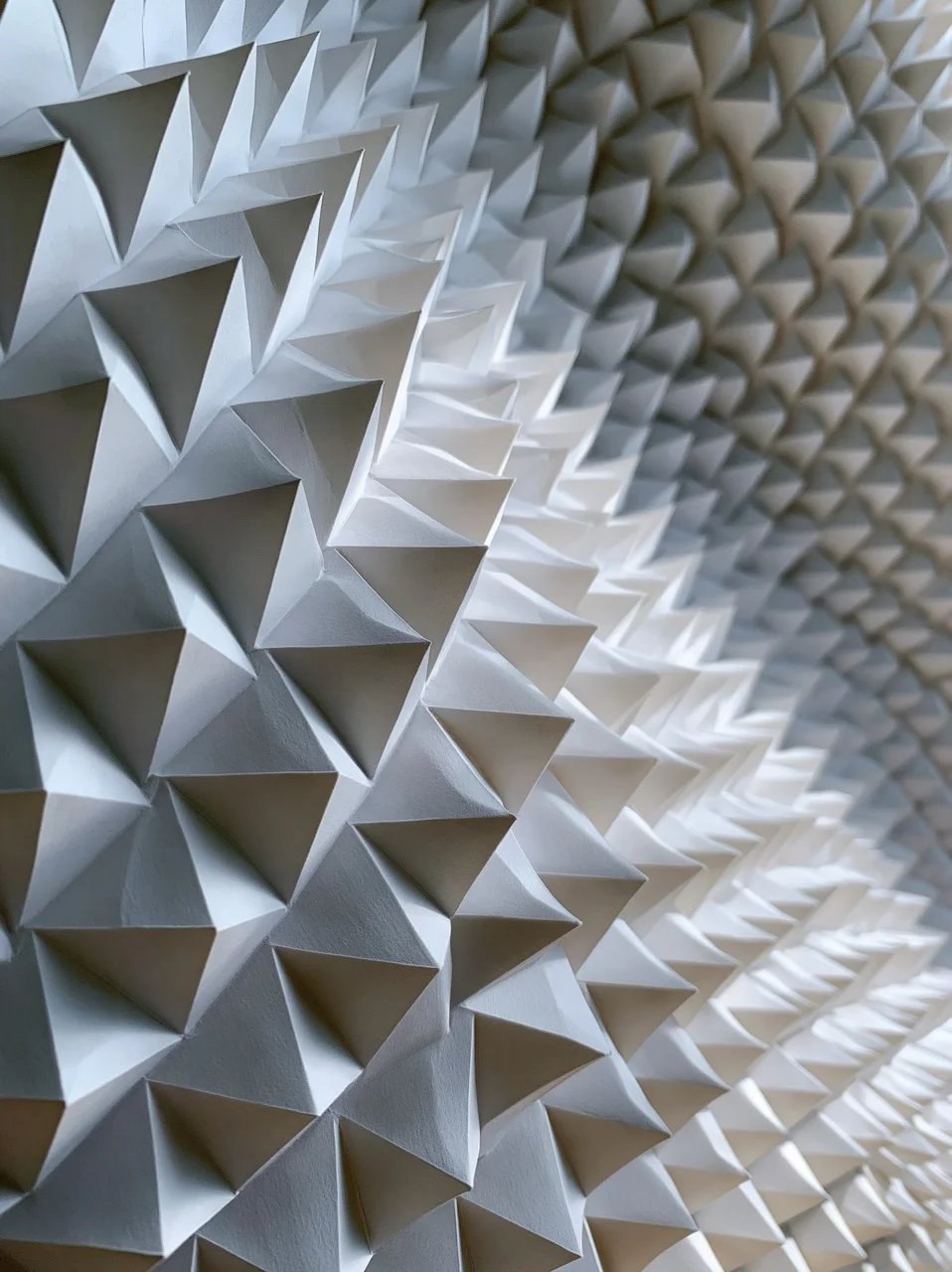 An abstract design featuring the visual repetition of delicate, folded white paper pyramids creating a wave-like pattern.