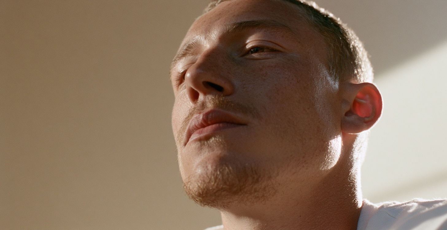 A close-up of a man's face in quiet contemplation, bathed in wrapped soft light against a warm beige background.